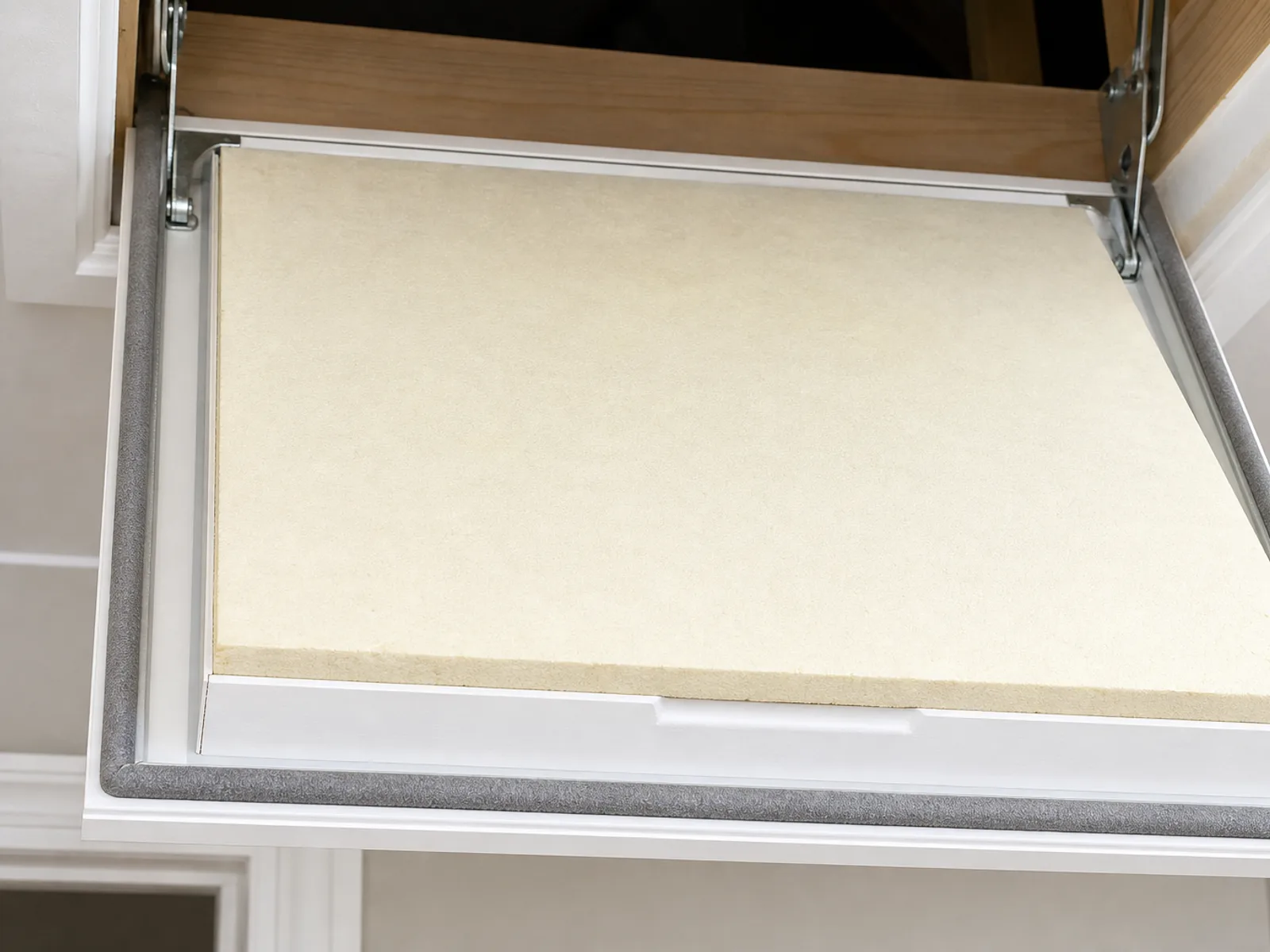 An open insulated loft hatch door showing thick insulation board on its upper face and the draught seal around the frame