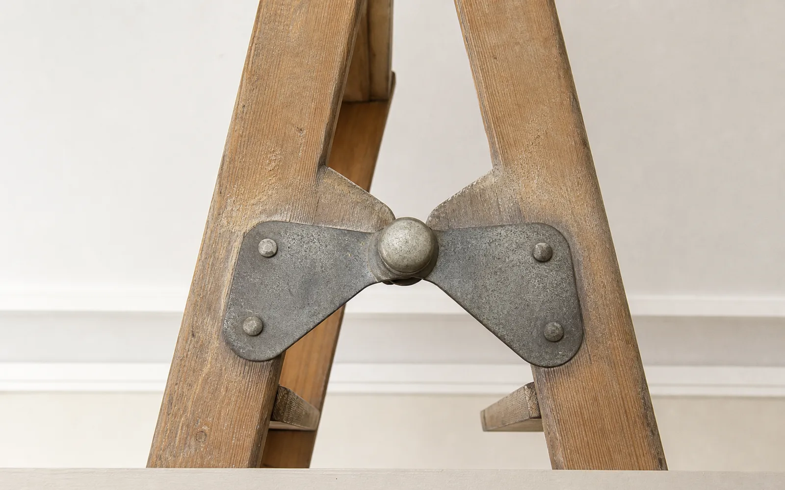 A worn pivot and hinge joint on a timber loft ladder, the metalwork dulled with use